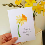 Happy Mother's Day card. Single daffodil hand printed with wooden stamps. Card held  in front of  bunch of daffodils